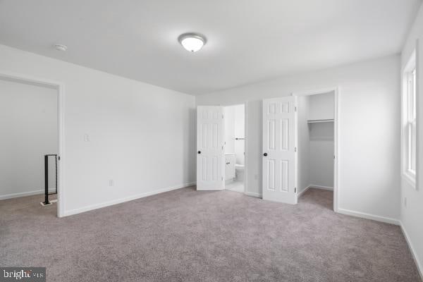 unfurnished bedroom featuring carpet floors, ensuite bath, a walk in closet, and a closet