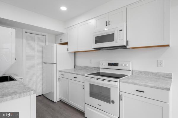 kitchen with white appliances, dark hardwood / wood-style floors, and white cabinets