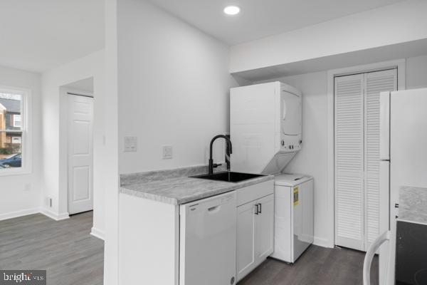 kitchen with stacked washing maching and dryer, white cabinetry, sink, dark hardwood / wood-style flooring, and white appliances