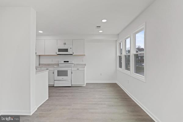 kitchen with white cabinetry, white appliances, and light hardwood / wood-style floors