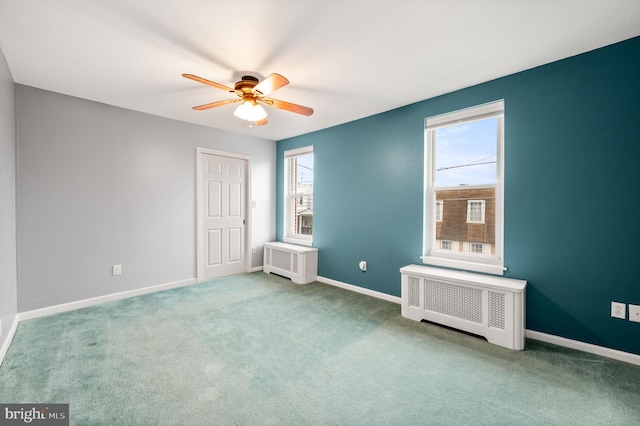 carpeted spare room with a wealth of natural light, radiator heating unit, and ceiling fan