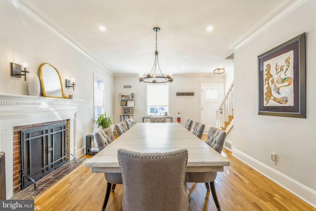 dining room with ornamental molding, a brick fireplace, a notable chandelier, and light hardwood / wood-style flooring