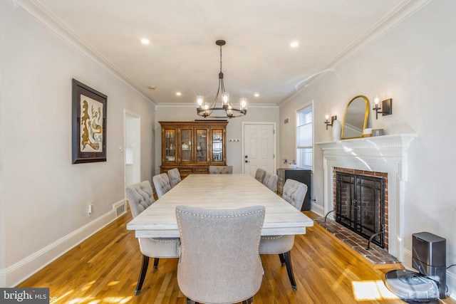 dining space featuring crown molding, a chandelier, hardwood / wood-style floors, and a brick fireplace