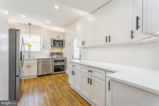 kitchen featuring white cabinetry, stainless steel appliances, light hardwood / wood-style floors, and hanging light fixtures