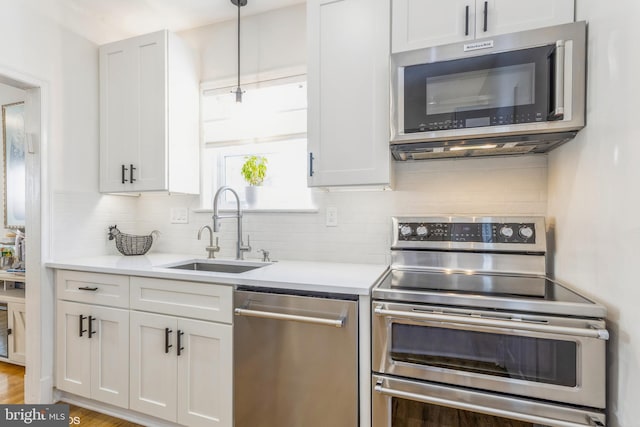 kitchen with pendant lighting, sink, appliances with stainless steel finishes, white cabinetry, and tasteful backsplash