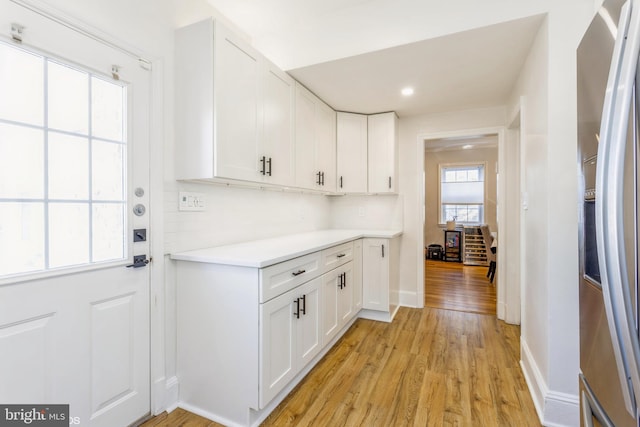 kitchen with white cabinetry, decorative backsplash, light hardwood / wood-style flooring, and stainless steel refrigerator with ice dispenser