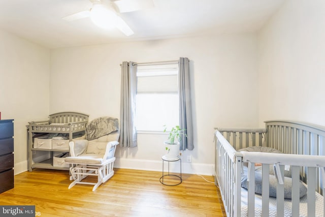 bedroom with a crib, hardwood / wood-style floors, and ceiling fan