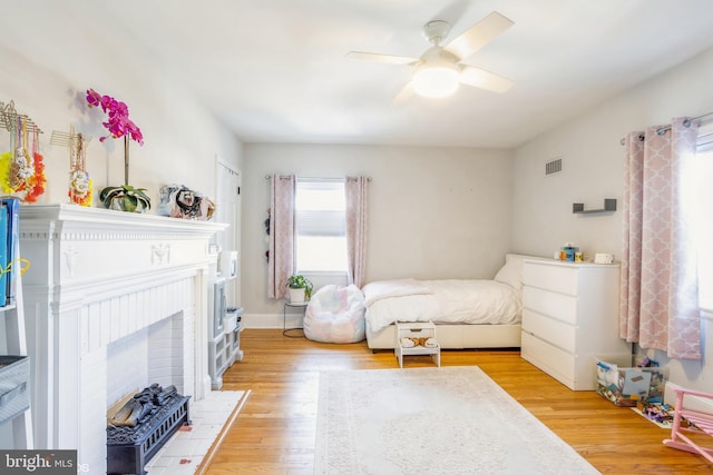 bedroom with a fireplace, light hardwood / wood-style flooring, and ceiling fan