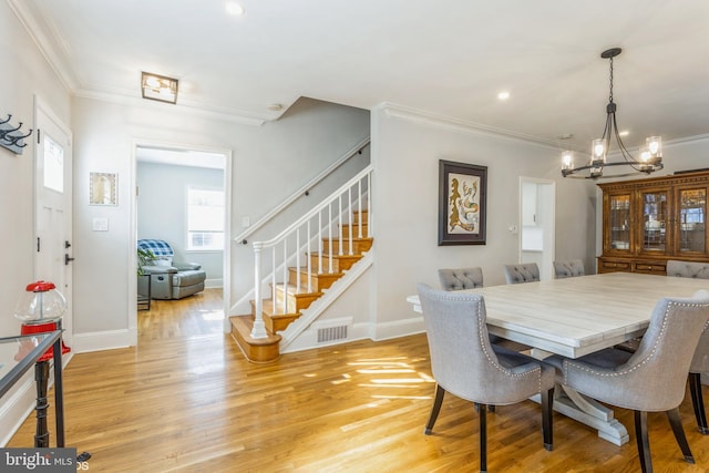 dining space with ornamental molding, an inviting chandelier, and light hardwood / wood-style flooring