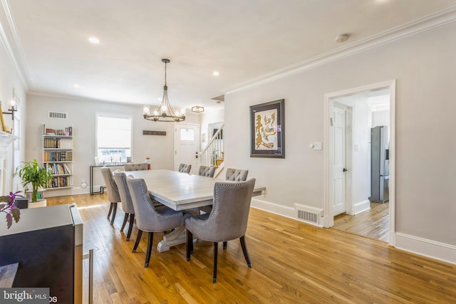 dining area with a notable chandelier, crown molding, and light hardwood / wood-style flooring