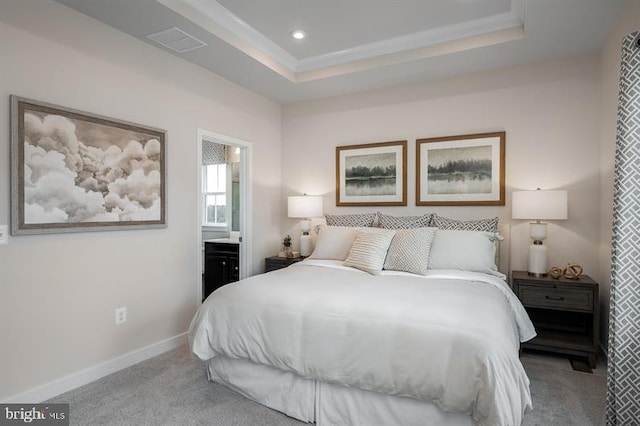 bedroom with light carpet, a raised ceiling, and ensuite bathroom