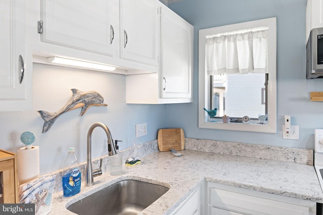 kitchen with white cabinetry, sink, and light stone counters