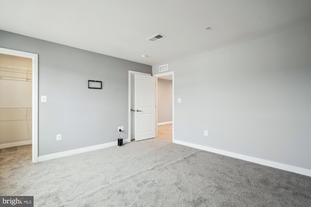 unfurnished bedroom featuring a walk in closet, light colored carpet, and a closet