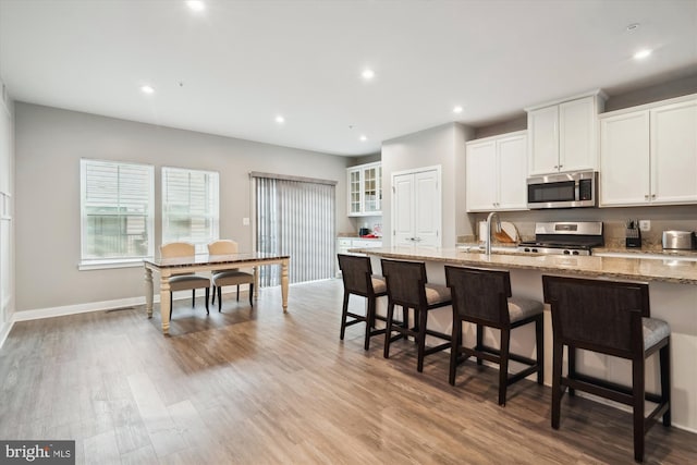 kitchen featuring light stone countertops, appliances with stainless steel finishes, a breakfast bar area, and white cabinets