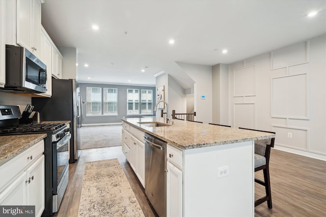 kitchen with sink, appliances with stainless steel finishes, a kitchen island with sink, a kitchen breakfast bar, and white cabinets