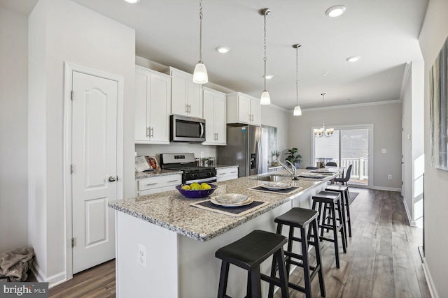 kitchen featuring a breakfast bar area, decorative light fixtures, a center island with sink, appliances with stainless steel finishes, and white cabinets