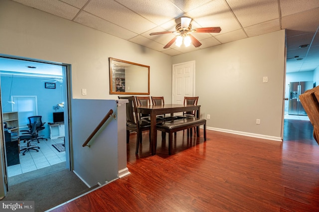 dining room with dark hardwood / wood-style floors, a drop ceiling, and ceiling fan