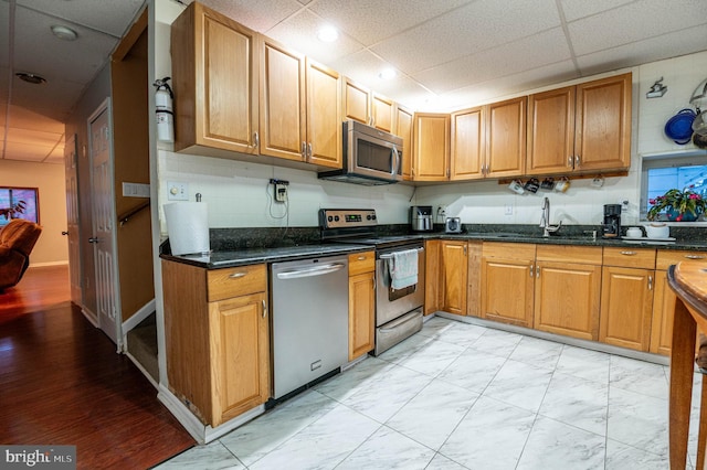 kitchen featuring sink, backsplash, appliances with stainless steel finishes, dark stone counters, and a drop ceiling