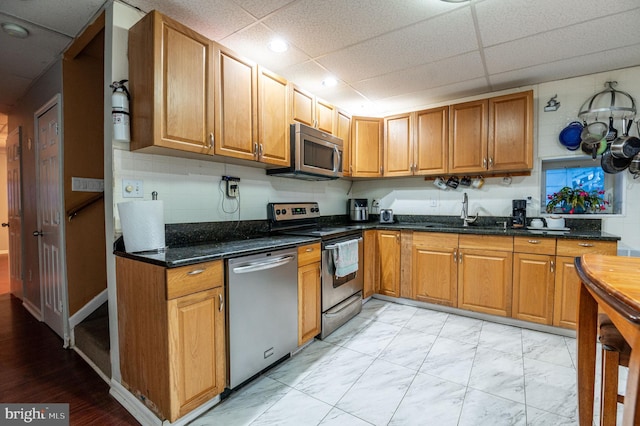 kitchen with a paneled ceiling, appliances with stainless steel finishes, sink, and dark stone counters