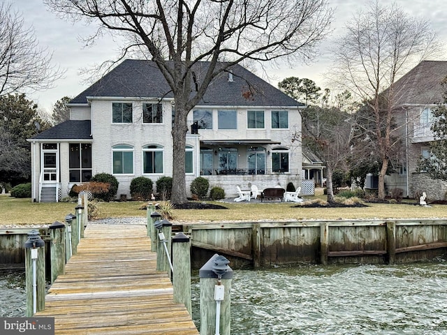 back of house featuring a water view, an outdoor fire pit, a sunroom, and a lawn