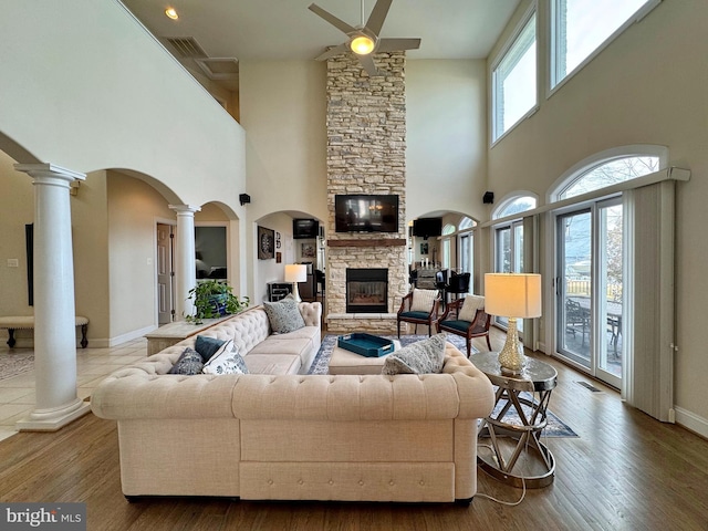 living room with a stone fireplace, wood-type flooring, ceiling fan, and ornate columns