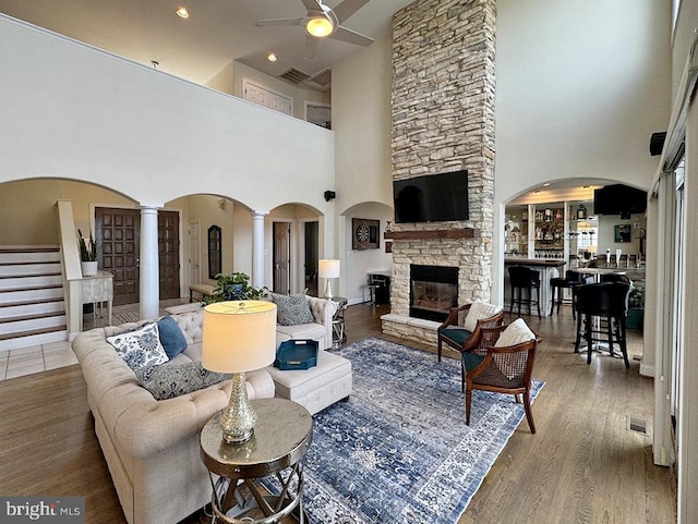 living room featuring ceiling fan, a stone fireplace, hardwood / wood-style floors, and ornate columns