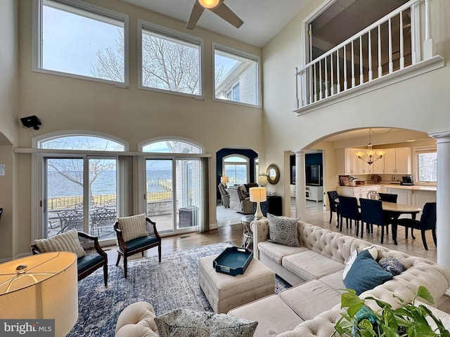 living room with a water view, ceiling fan with notable chandelier, decorative columns, and hardwood / wood-style floors