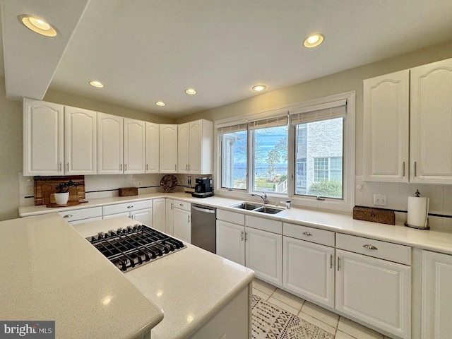 kitchen featuring stainless steel dishwasher, light tile patterned floors, sink, and white cabinets