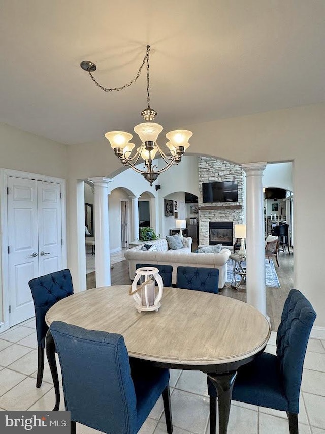 dining room featuring ornate columns, a chandelier, light tile patterned floors, and a fireplace