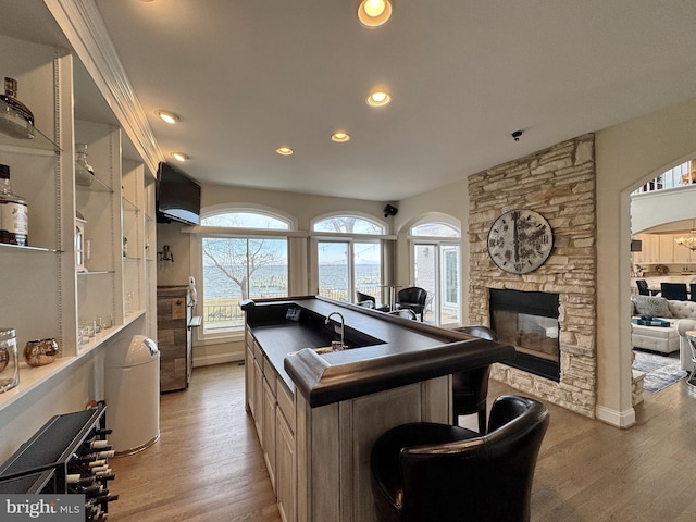 kitchen with a kitchen bar, a stone fireplace, light hardwood / wood-style floors, and a center island with sink