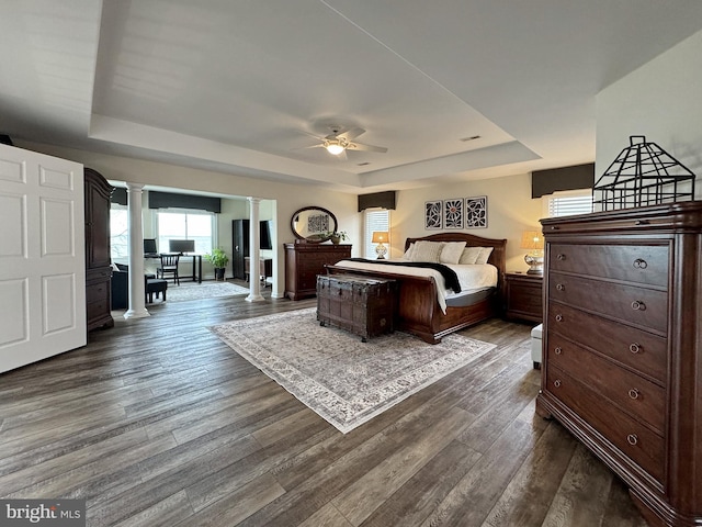 bedroom featuring a tray ceiling, dark wood-type flooring, and decorative columns