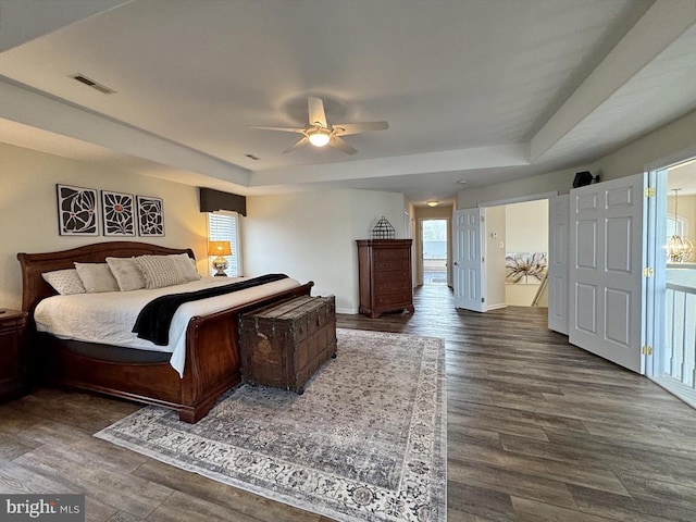 bedroom with dark hardwood / wood-style flooring, a tray ceiling, and ceiling fan