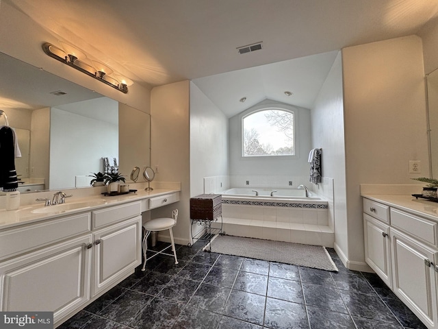 bathroom featuring tiled tub, vaulted ceiling, and vanity