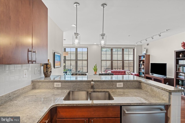 kitchen with light stone countertops, a sink, open floor plan, stainless steel dishwasher, and brown cabinets