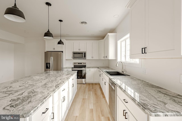 kitchen with appliances with stainless steel finishes, sink, white cabinets, and decorative light fixtures