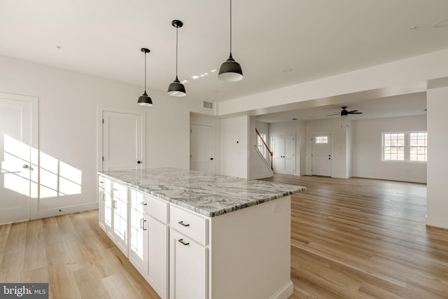 kitchen featuring decorative light fixtures, white cabinets, a center island, light stone counters, and light hardwood / wood-style flooring