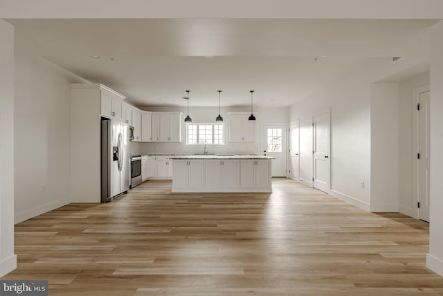 kitchen with pendant lighting, light hardwood / wood-style flooring, appliances with stainless steel finishes, a center island, and white cabinets