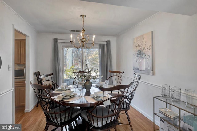 dining space featuring an inviting chandelier, ornamental molding, and light wood-type flooring