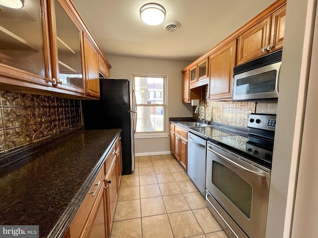 kitchen with light tile patterned flooring, appliances with stainless steel finishes, sink, dark stone countertops, and decorative backsplash