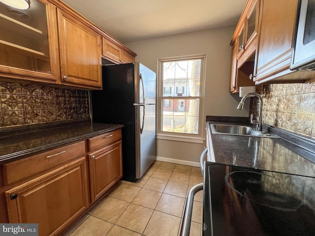 kitchen with sink, light tile patterned floors, stainless steel fridge, dark stone counters, and decorative backsplash