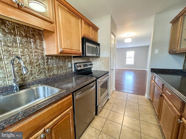 kitchen featuring sink, light tile patterned floors, appliances with stainless steel finishes, dark stone counters, and backsplash