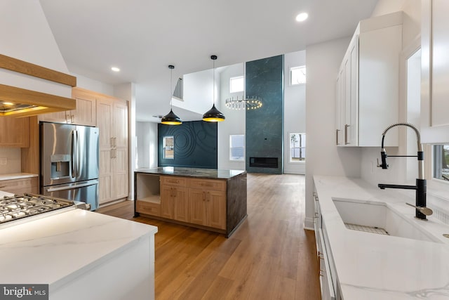 kitchen with hanging light fixtures, sink, white cabinets, and stainless steel fridge