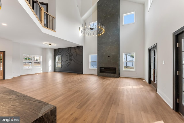 living room with a high ceiling, wood-type flooring, an inviting chandelier, and a high end fireplace