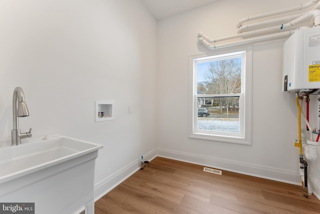 clothes washing area featuring sink, hookup for a washing machine, light hardwood / wood-style flooring, and tankless water heater