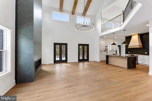 living room featuring beamed ceiling, a healthy amount of sunlight, light wood-type flooring, and french doors