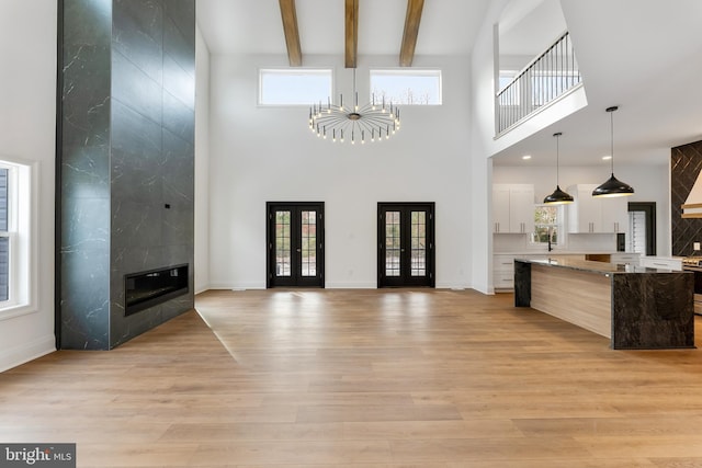 living room with a fireplace, a chandelier, light hardwood / wood-style floors, beam ceiling, and french doors