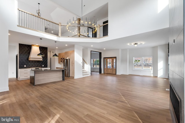 unfurnished living room featuring wood-type flooring, a high ceiling, and a notable chandelier