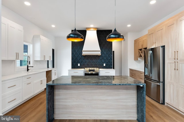 kitchen with appliances with stainless steel finishes, white cabinetry, a center island, custom range hood, and decorative light fixtures