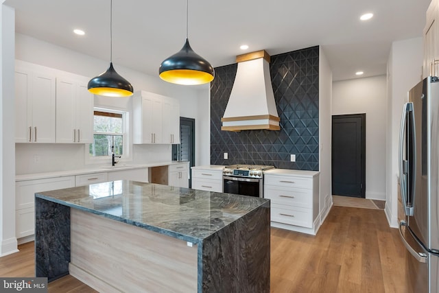 kitchen featuring appliances with stainless steel finishes, dark stone countertops, white cabinets, decorative light fixtures, and custom exhaust hood