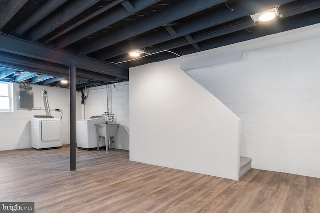 basement featuring washer and clothes dryer, sink, wood-type flooring, and electric panel